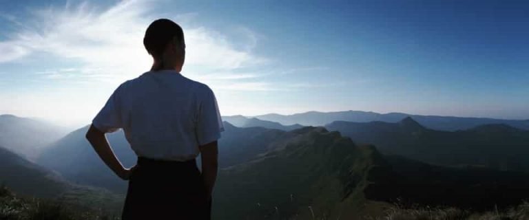 Sur une colline, une personne regarde des montagnes au soleil sous un ciel bleu, illustrant la Gestalt-thérapie.