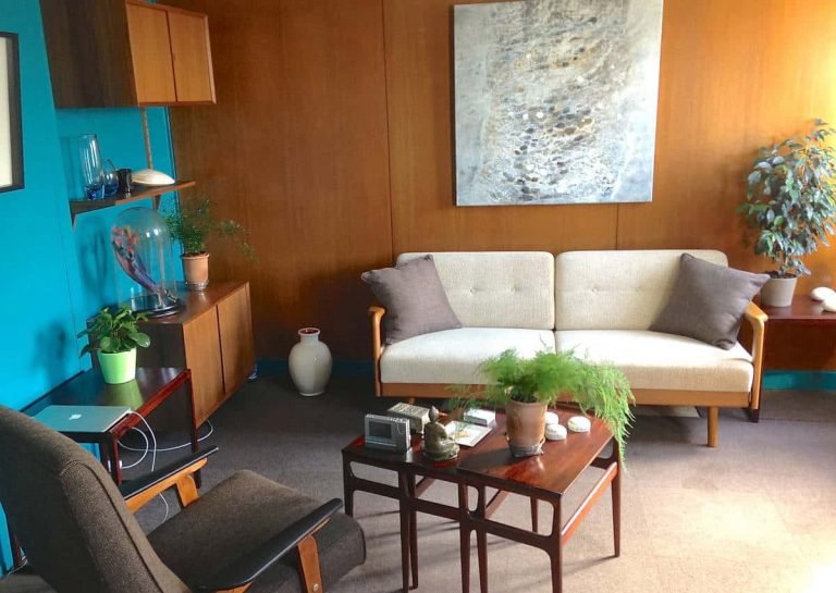 Salon lumineux style mid-century avec canapé crème, plantes vertes, mur bleu canard, idéal pour formation Gestalt.
