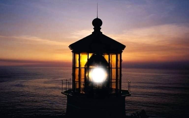 Un phare à la lumière éclatante se détache sur un ciel coloré de coucher de soleil, surplombant un océan calme - une image qui fait écho à la perspective holistique de la Gestalt thérapie, alors que le soir tombe et que le ciel passe de l'orange au violet.