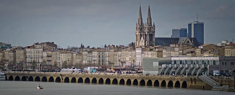 Une vue panoramique de Bordeaux, en France, montrant des bâtiments historiques au bord de la rivière, un long pont en pierre sur la Garonne et les flèches de la cathédrale Saint-André - une scène inspirante pour toute personne intéressée par la Gestalt ou poursuivant une formation de praticien en Gestalt.