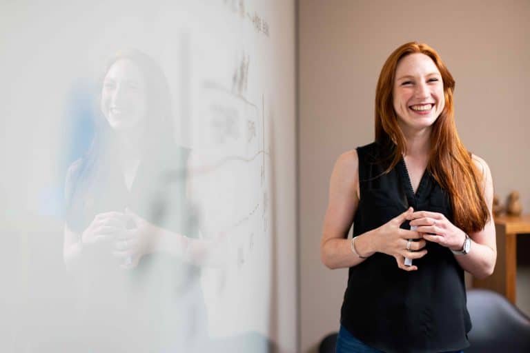 Une femme fait une présentation devant un tableau blanc.
