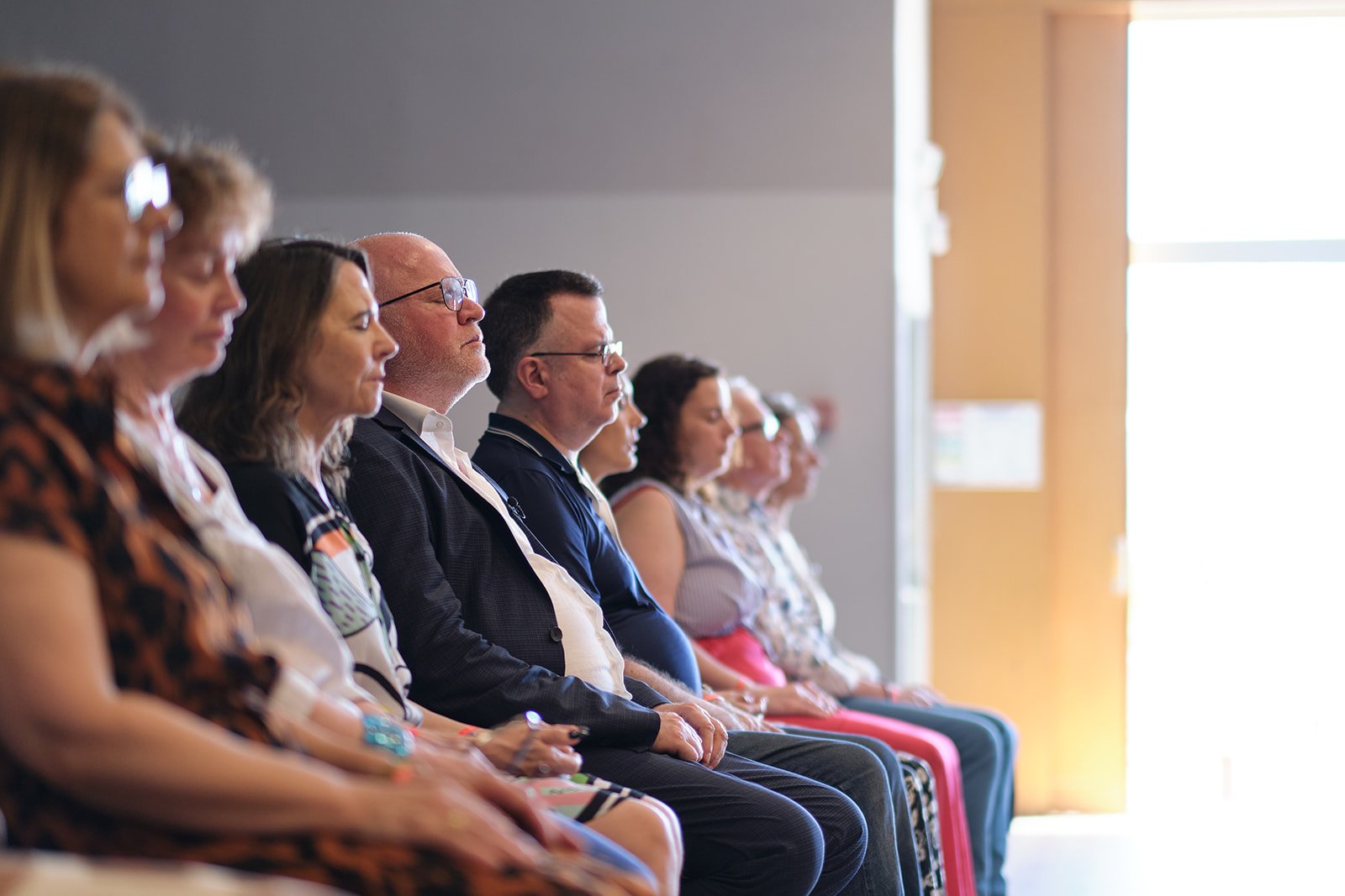 Groupe assis côte à côte en intérieur, yeux fermés, mains sur les genoux, ambiance douce lors d'une séance de Gestalt-thérapie.