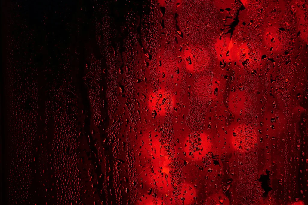 Gouttes d'eau sur une vitre, lumière rouge traversante et flou bokeh en arrière-plan pour la Gestalt-thérapie.