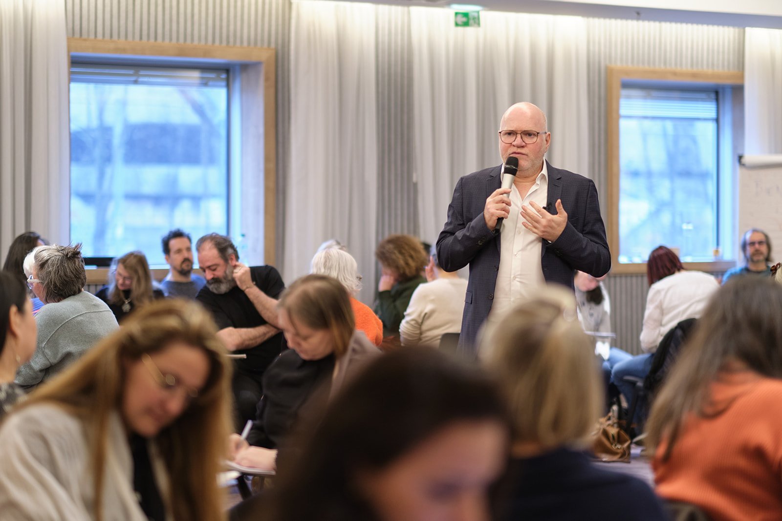 Conférencier en costume intervenant au micro devant un public attentif lors d'une formation Gestalt-thérapie.