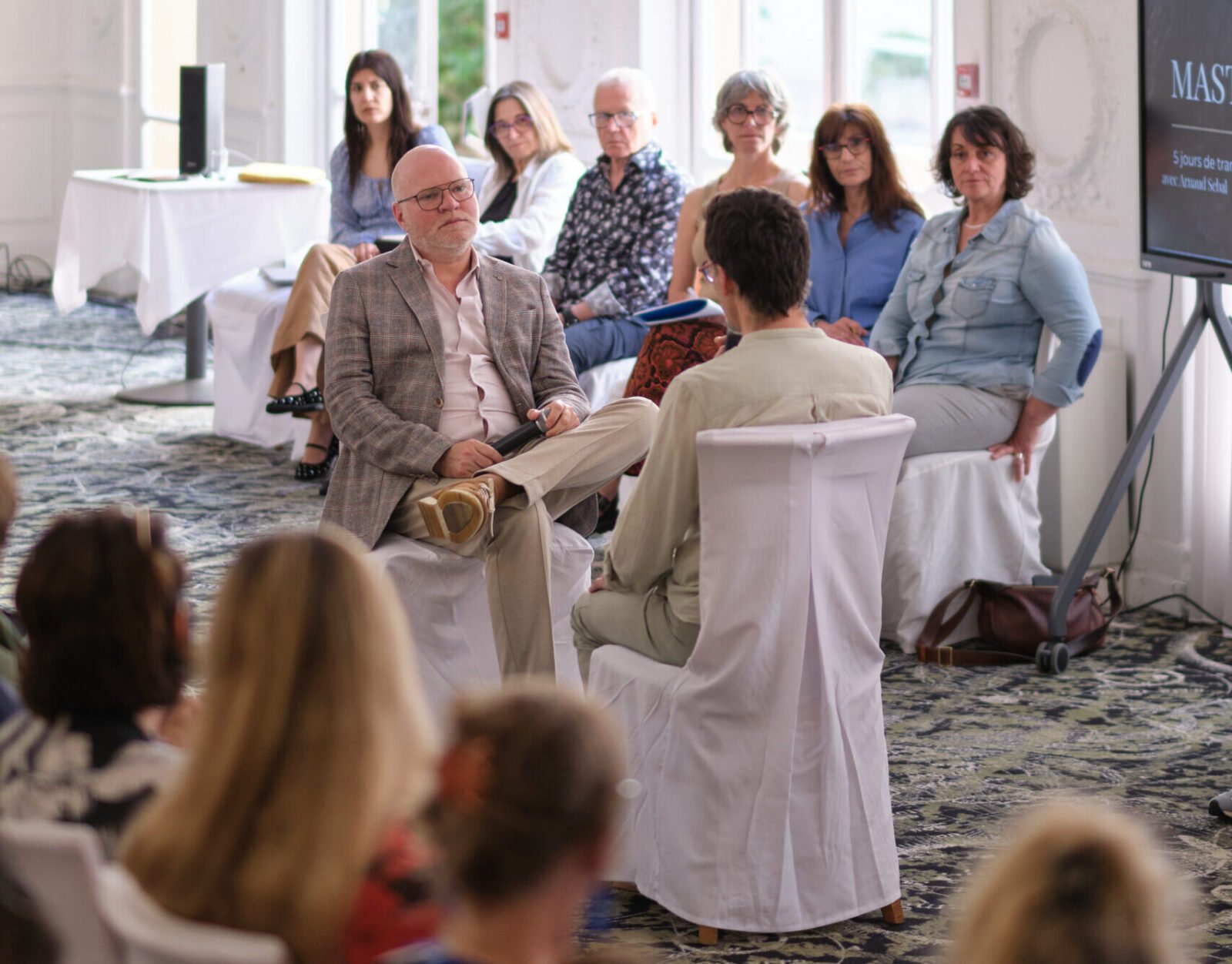 Participants assis dans une salle lumineuse discutent reconversion ; écran à droite, public attentif, formation Gestalt.