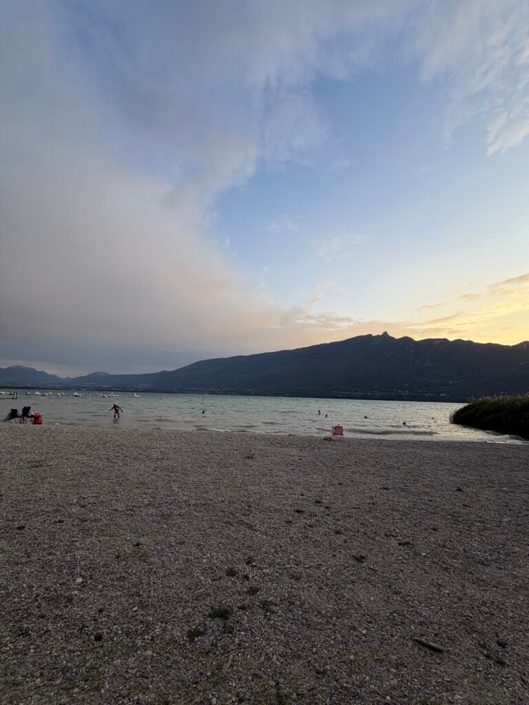 Plage de galets au soir, montagnes et nuages au loin