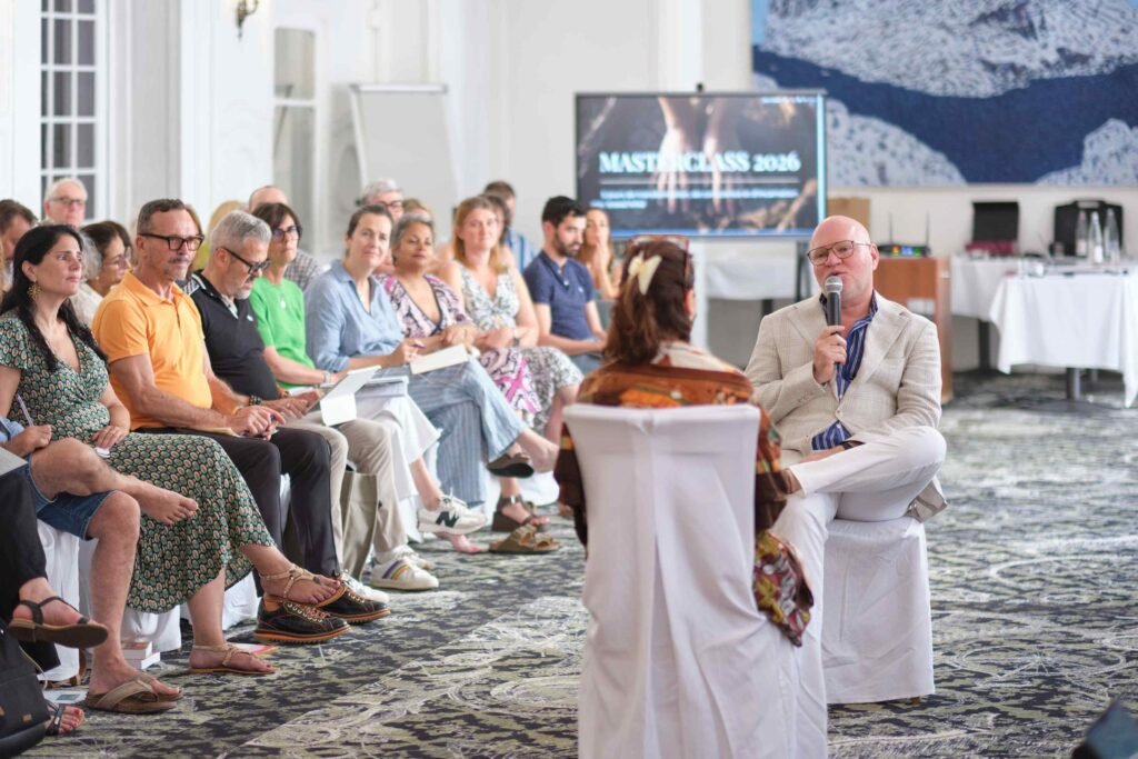 Groupe en demi-cercle lors d’un atelier de formation en thérapie Gestalt ; un homme anime la discussion sur l’estime de soi. À l’écran : MASTERCLASS 2026.